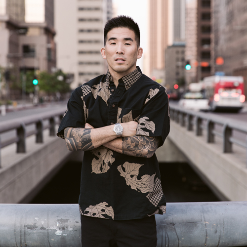 Tim Hirata in an aloha shirt, arms crossed, on a downtown Los Angeles bridge