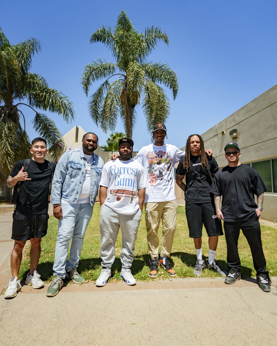 Six men standing together on a lawn with palm trees