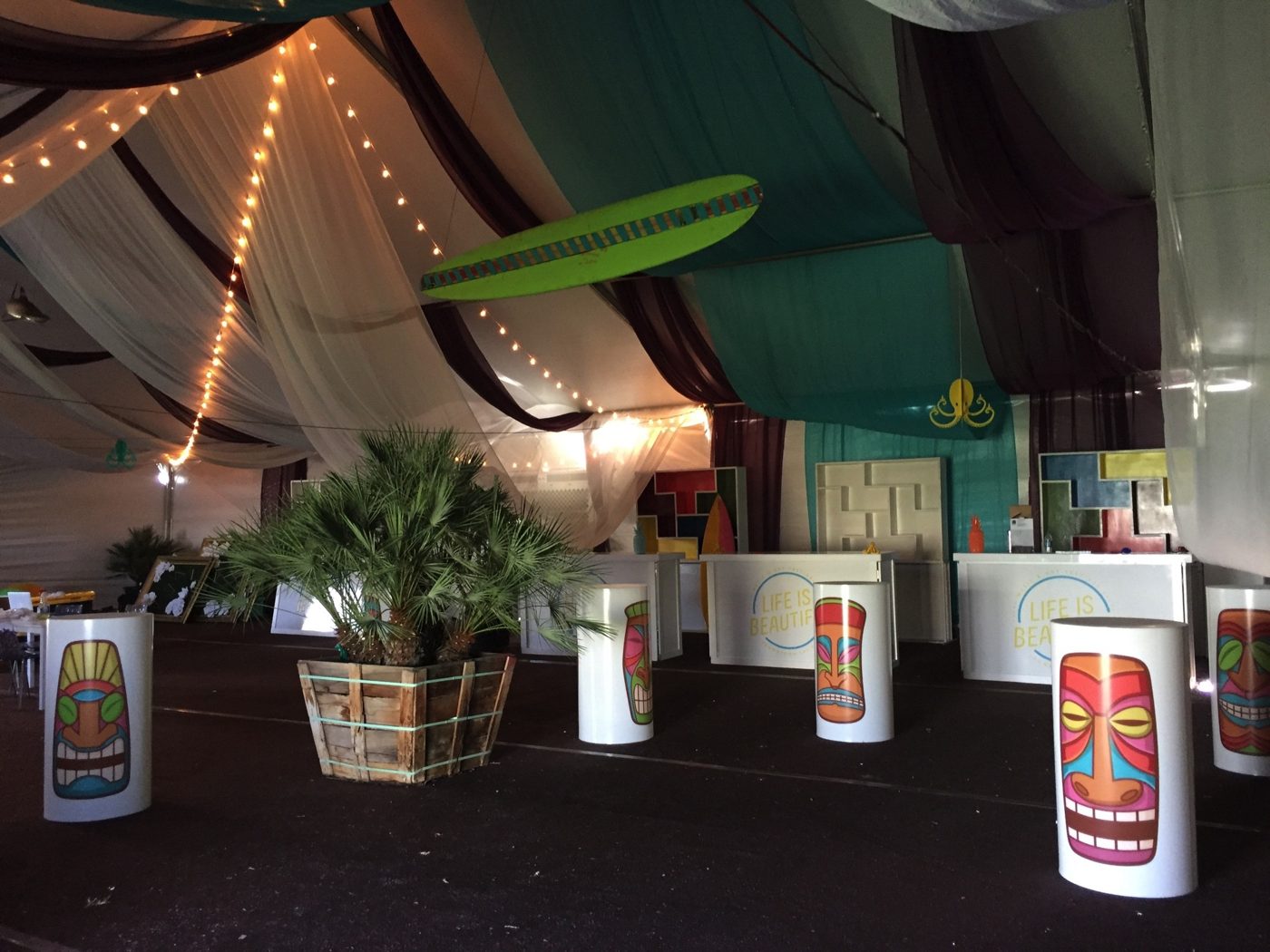 The empty artist VIP tent with tiki-mask tables and a surfboard overhead, before the festival
